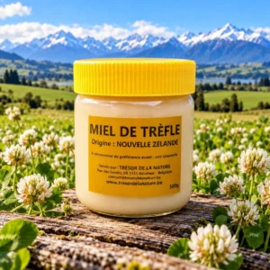 Miel de trèfle de Nouvelle-Zélande 500 g – Prairie fleurie Pot de miel de trèfle de Nouvelle-Zélande 500 g entouré de trèfles en fleurs, avec des montagnes en arrière-plan